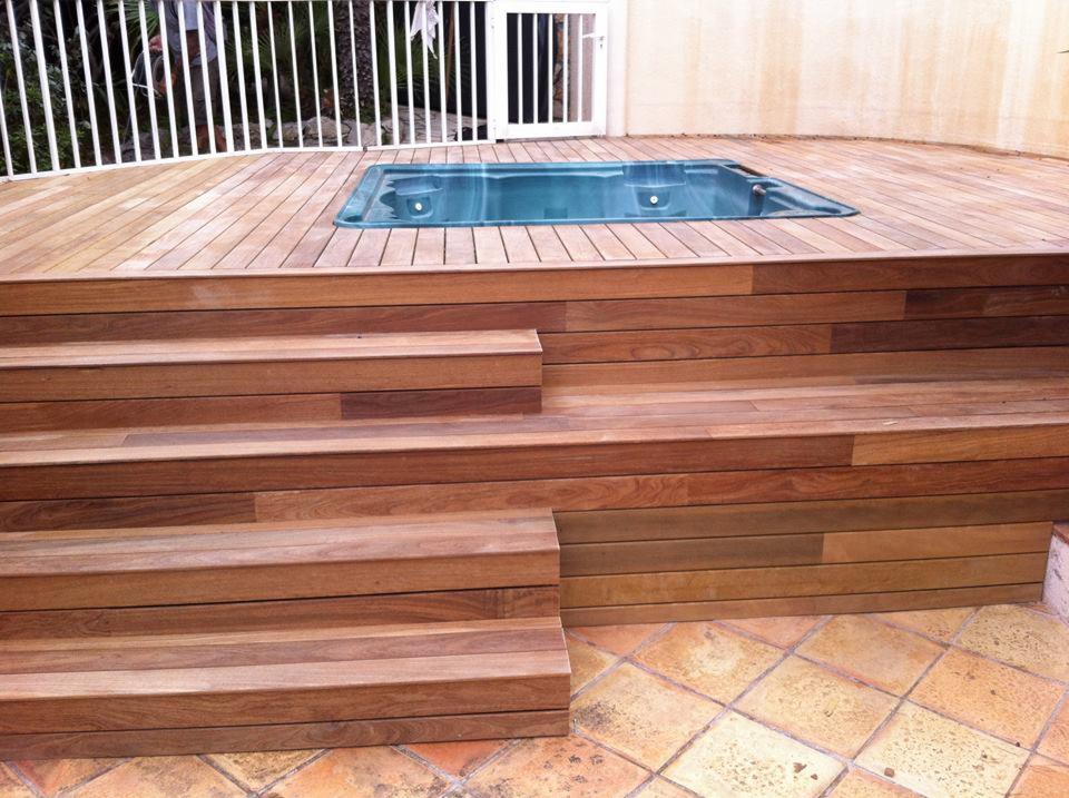 Drewniany taras z jacuzzi i schodami w Jasionce, wykonany z desek o ciepłym odcieniu brązu, otoczony białym ogrodzeniem i terakotową podłogą.