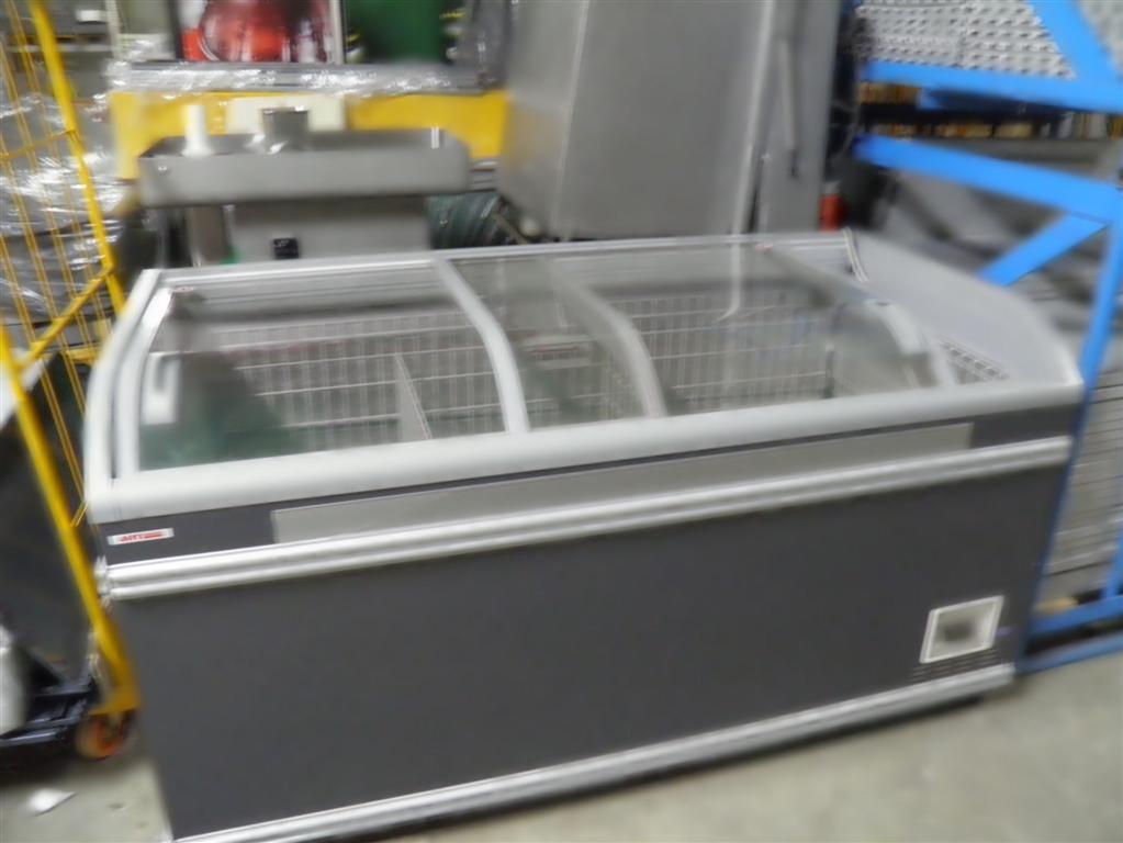 Zamrażarka skrzyniowa z przeszkloną pokrywą w szarym kolorze, widoczna w magazynie lub sklepie, z wózkiem transportowym obok.
