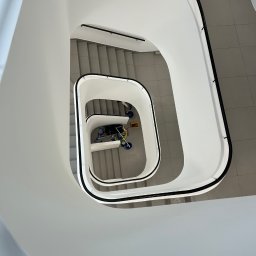 SOLIDTRANS-TEAM ILONA ARCISZEWSKA - Spiralne schody z widokiem z góry na wózek do sprzątania na podeście. Minimalistyczna architektura wnętrza w jasnych barwach.