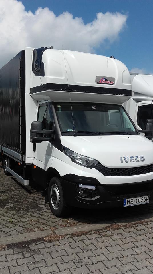 Biały bus dostawczy Iveco z czarną plandeką na parkingu, widoczny numer rejestracyjny WB 1825M.