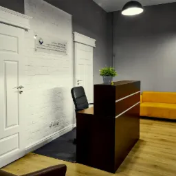 Nowoczesne wnętrze kancelarii prawnej z recepcją, żółtą sofą i ścianą z białej cegły z tabliczką informacyjną.