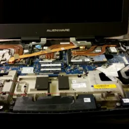 Otwarty laptop Alienware z widoczną płytą główną, układem chłodzenia i innymi komponentami wewnętrznymi, obok leży sprężone powietrze w puszce i narzędzia.