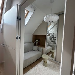 Mieszkanie w Twoim stylu - Kompaktowa aranżacja pod skosem: sofa, stolik i lustro powiększające przestrzeń w jasnym wnętrzu z akcentem drewna i dekoracyjną tapetą.