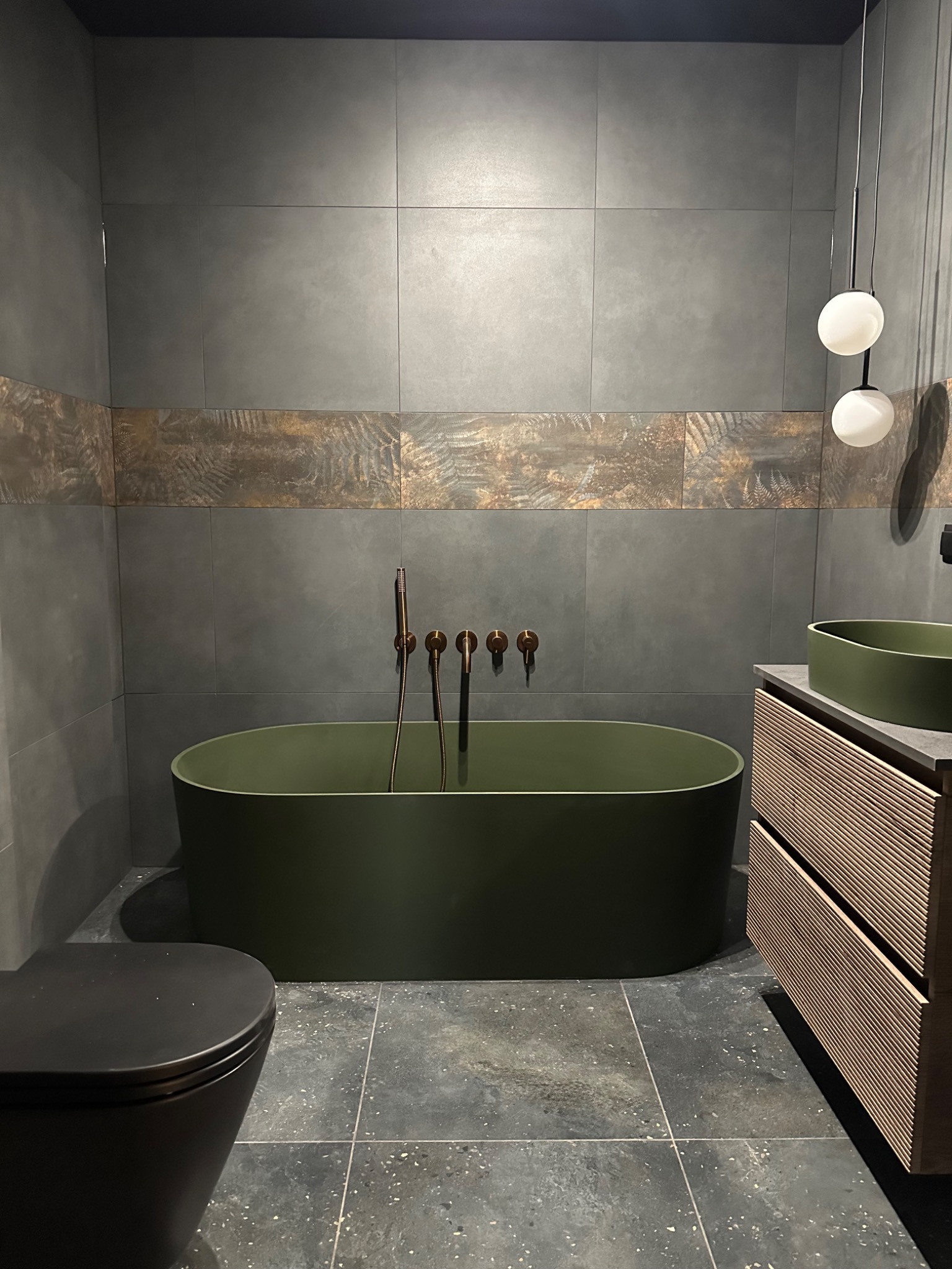 Nowoczesna łazienka z oliwkową wanną i umywalką. Szare płytki z dekoracyjnym pasem. Armatura w kolorze mosiądzu. Minimalistyczne oświetlenie.