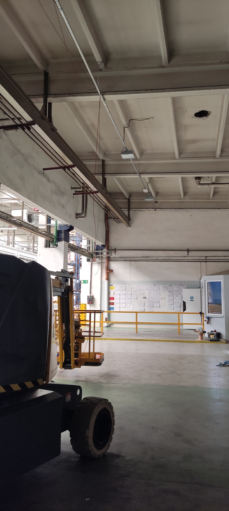 Wnętrze hali przemysłowej z widocznymi przewodami i elementami instalacji pod sufitem, platforma robocza na pierwszym planie.