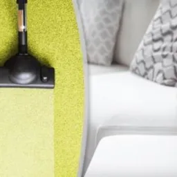 Czyszczenie zielonego dywanu odkurzaczem z widocznym efektem odświeżenia, obok fragment białej sofy z dekoracyjnymi poduszkami w szaro-białe wzory.