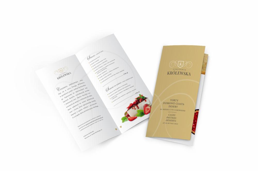 Rozłożona broszura reklamowa cukierni Królewska, prezentująca ofertę tortów, ciast domowych i deserów, z widocznym menu i zdjęciem deseru truskawkowego.