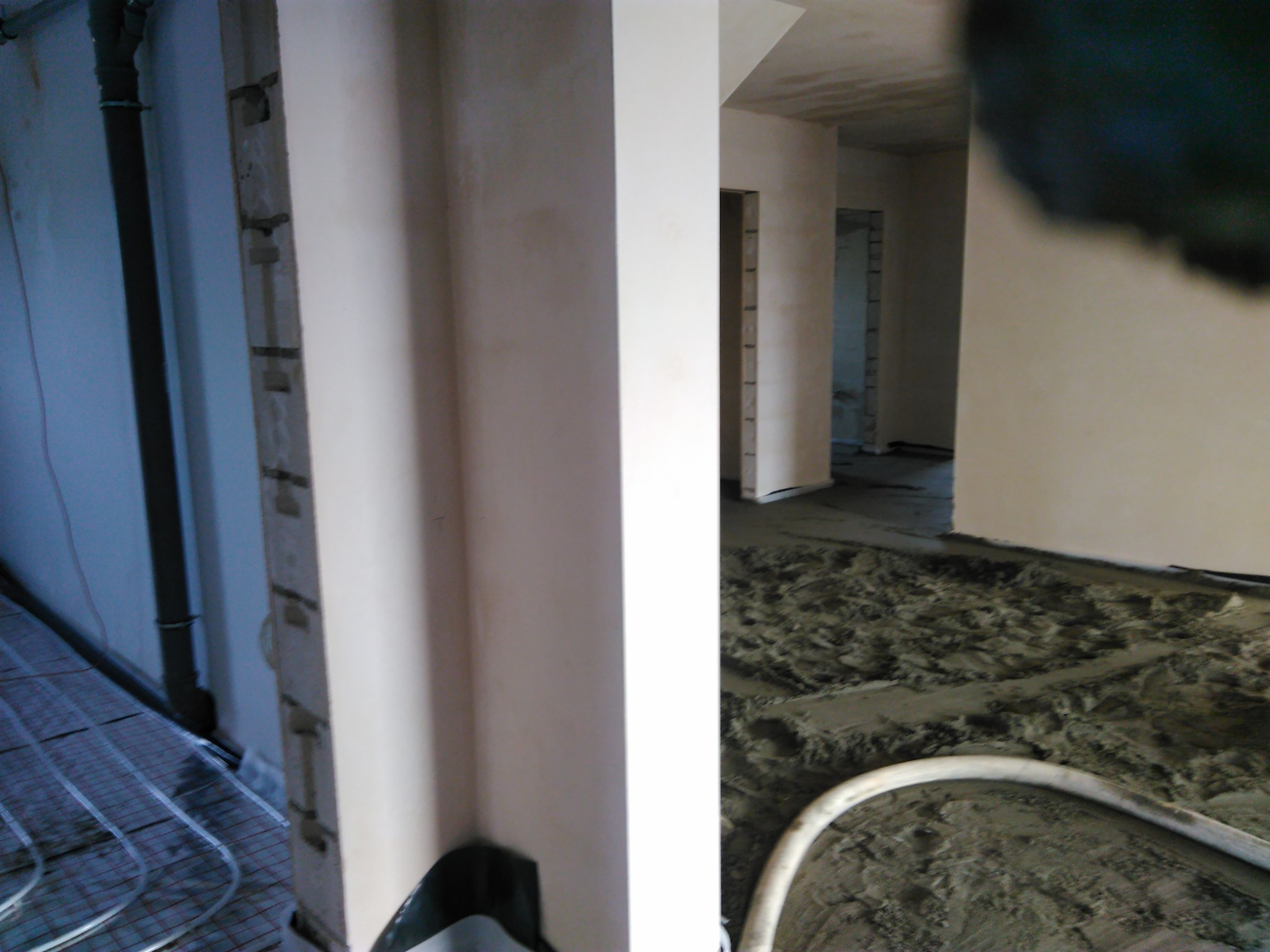 Wylewanie posadzki jastrychowej z widocznym systemem ogrzewania podłogowego, rurą doprowadzającą mieszankę i surowymi ścianami w tle.