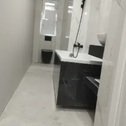 Nowoczesna łazienka w trakcie wykańczania, z marmurowymi płytkami na ścianach i podłodze, czarną armaturą i podwieszaną toaletą, widoczne niedokończone prace na podłodze.