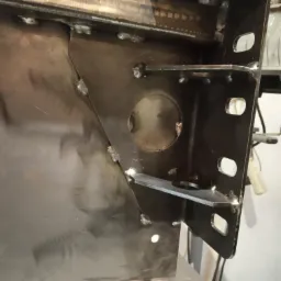 Spawana konstrukcja stalowa z widocznymi spawami, otworem i elementami mocującymi, surowy metal bez obróbki wykończeniowej.