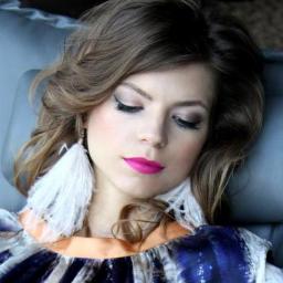 Fabryka Urody - Portret kobiety z zamkniętymi oczami, w profesjonalnym makijażu z różowymi ustami, podkreślonymi oczami i dużymi, białymi kolczykami z piór.