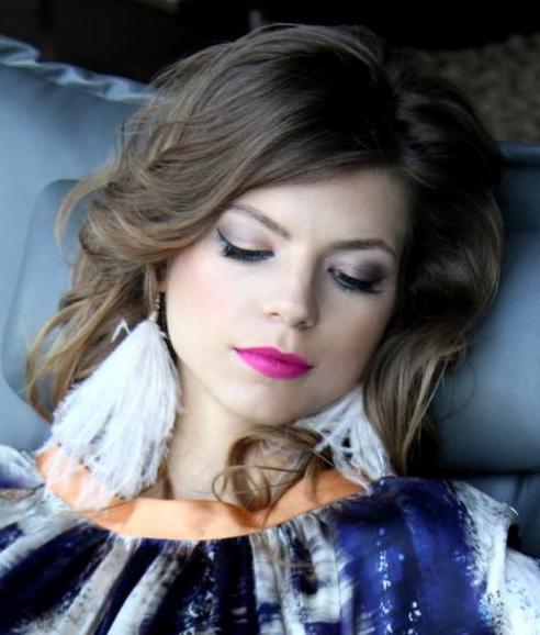 Portret kobiety z zamkniętymi oczami, w profesjonalnym makijażu z różowymi ustami, podkreślonymi oczami i dużymi, białymi kolczykami z piór.