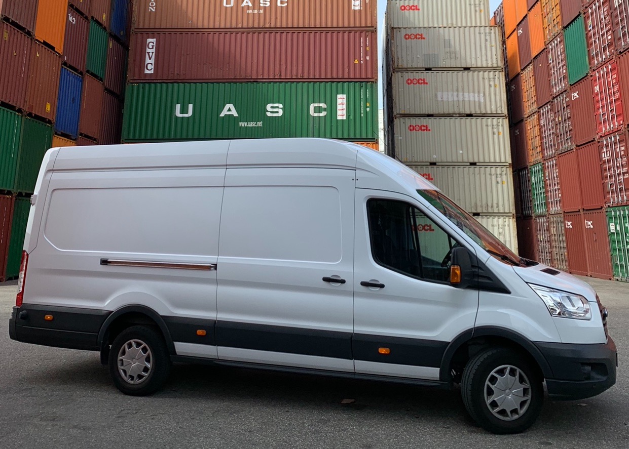 Biały furgon dostawczy marki Ford Transit na tle kolorowych kontenerów transportowych, widok z boku.