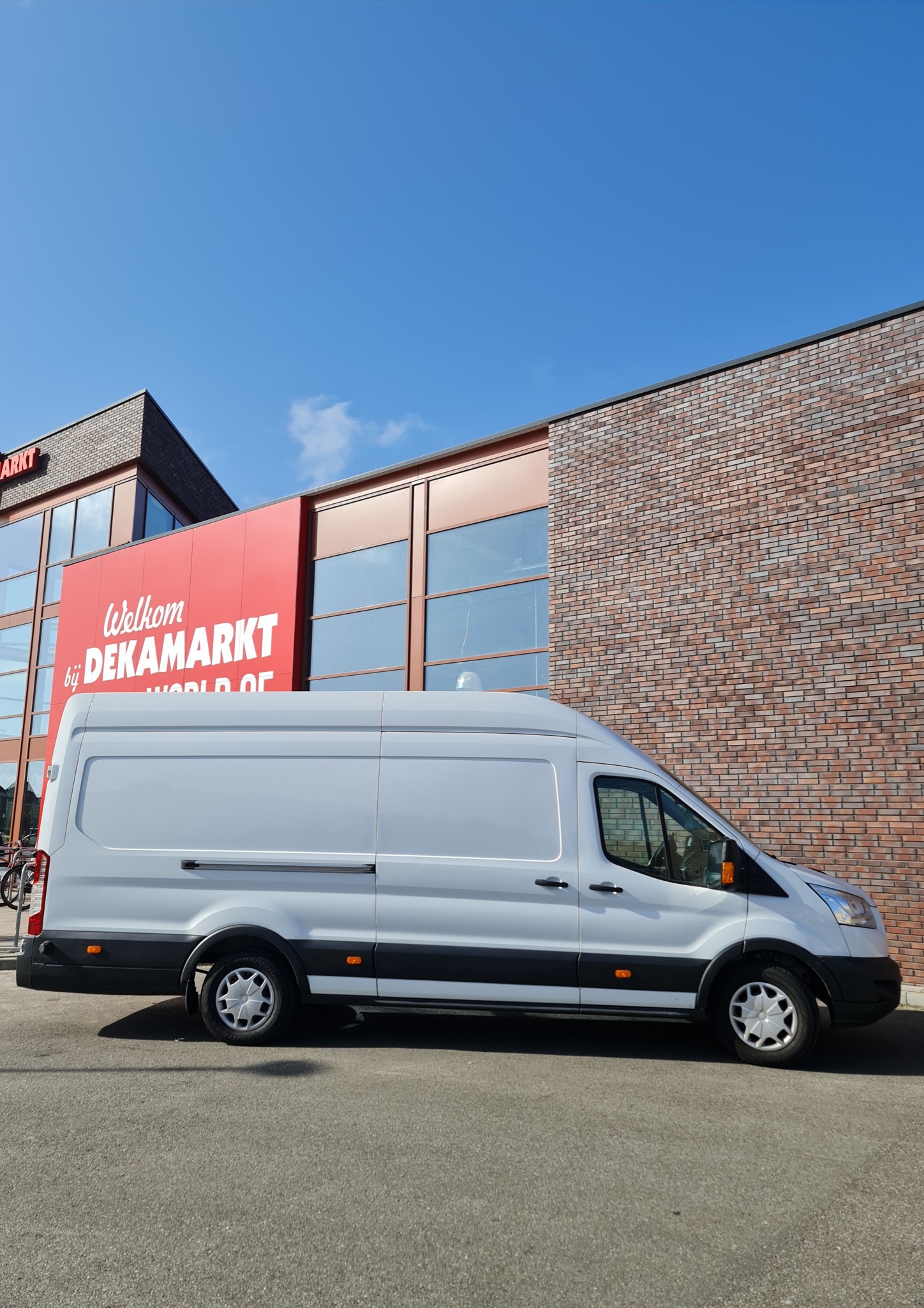 Biały van zaparkowany przed budynkiem Dekamarkt w słoneczny dzień.