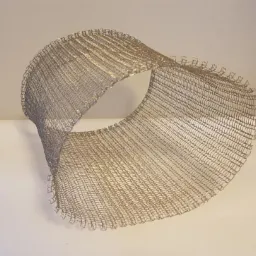 Elastyczny fragment metalowej siatki ogrodzeniowej zwinięty w cylinder, prezentowany na białym tle.