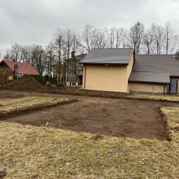 PIOTRO-TRANS Piotr Ostasiewicz - Wykopane fundamenty pod budynek, widoczny wykop, pracownik i koparka w tle, pochmurne niebo.