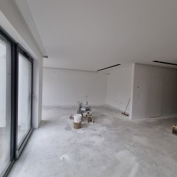 DHM Marcin Lewczuk - Przygotowanie do malowania natryskowego w przestronnym wnętrzu w Głogowie. Widoczne narzędzia i sprzęt malarski, surowy beton na podłodze, duże okno.