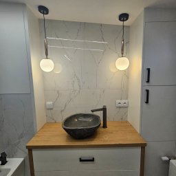 DHM Marcin Lewczuk - Nowoczesna łazienka z kamienną umywalką, drewnianym blatem i marmurowymi płytkami. Dwie okrągłe lampy wiszące dodają elegancji. Minimalistyczny design.