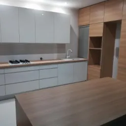 Nowoczesna kuchnia z szarymi frontami szafek i drewnianym blatem, widoczna płyta gazowa oraz wyspa kuchenna z blatem w kolorze drewna.