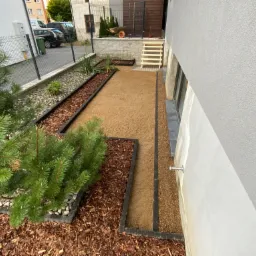 Przygotowany teren pod przyszły ogród z wydzielonymi rabatami, wysypany korą i piaskiem, widoczne schody prowadzące do ogrodu.