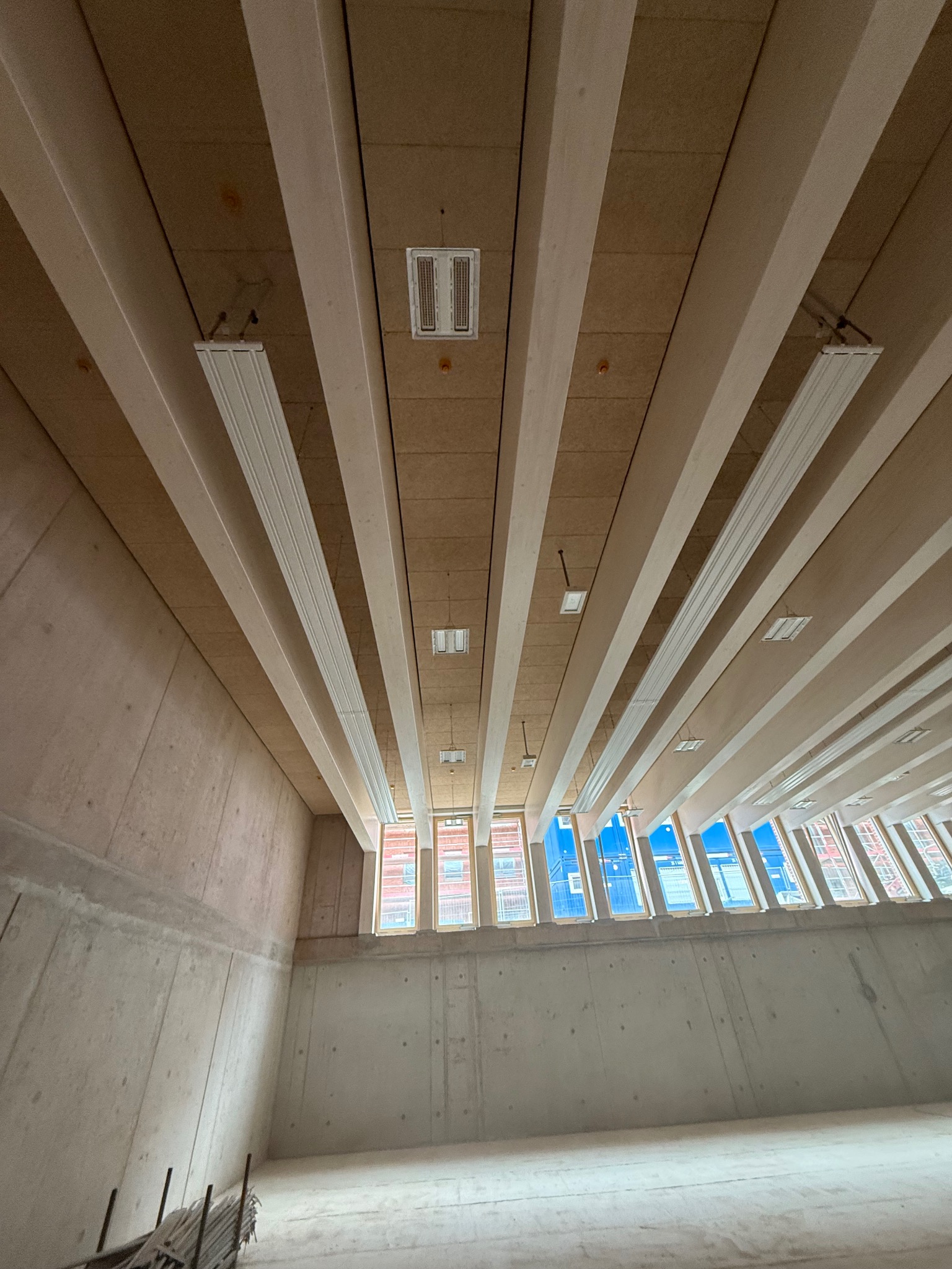 Surowe wnętrze z betonowymi ścianami i drewnianym stropem z belkami oraz oknami w górnej części ściany, widok z dołu.