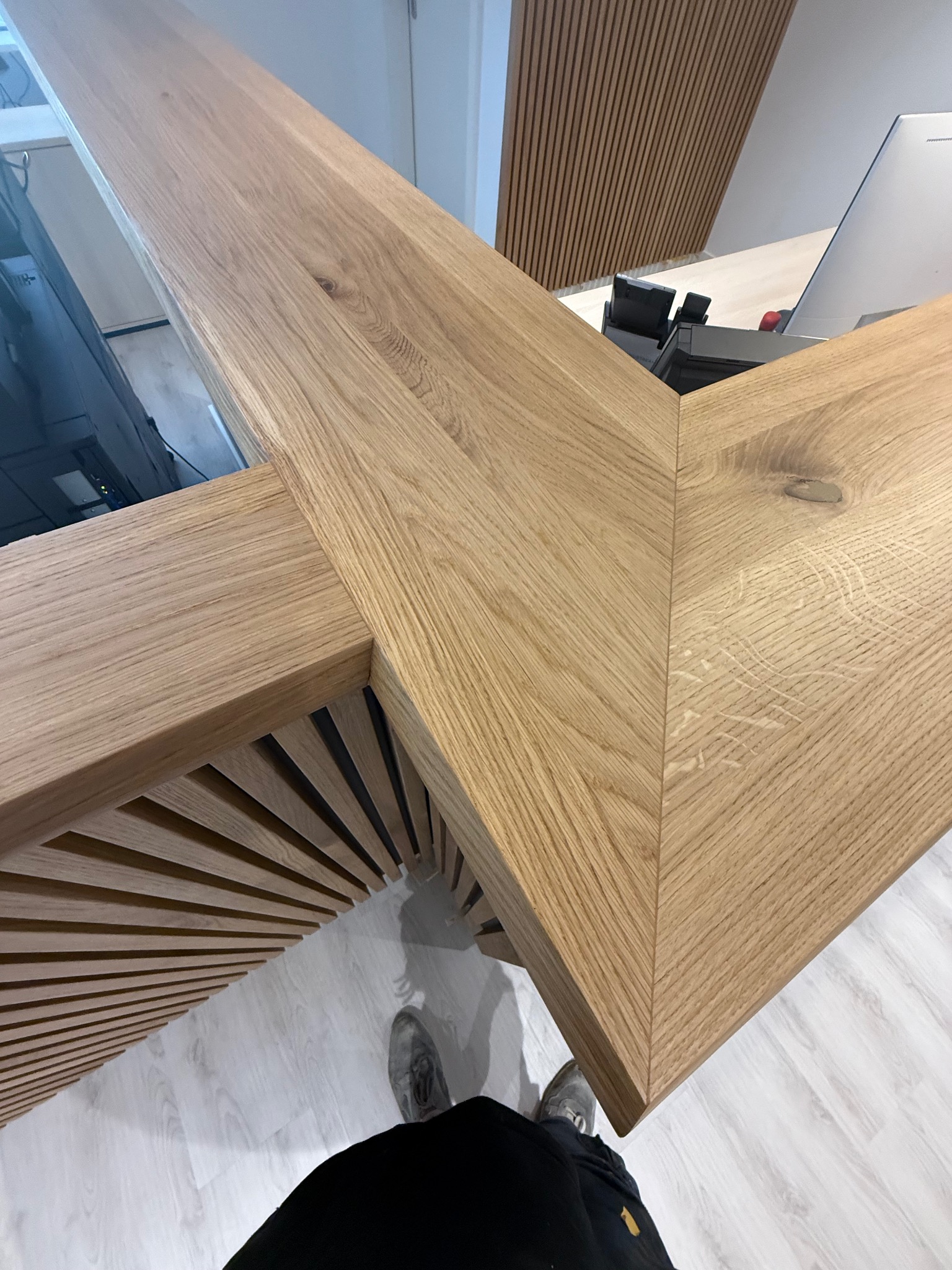 Detal drewnianej konstrukcji z bliska, ukazujący precyzyjne połączenie elementów i naturalny rysunek drewna. Widoczne elementy biurka i dekoracji ściennych.