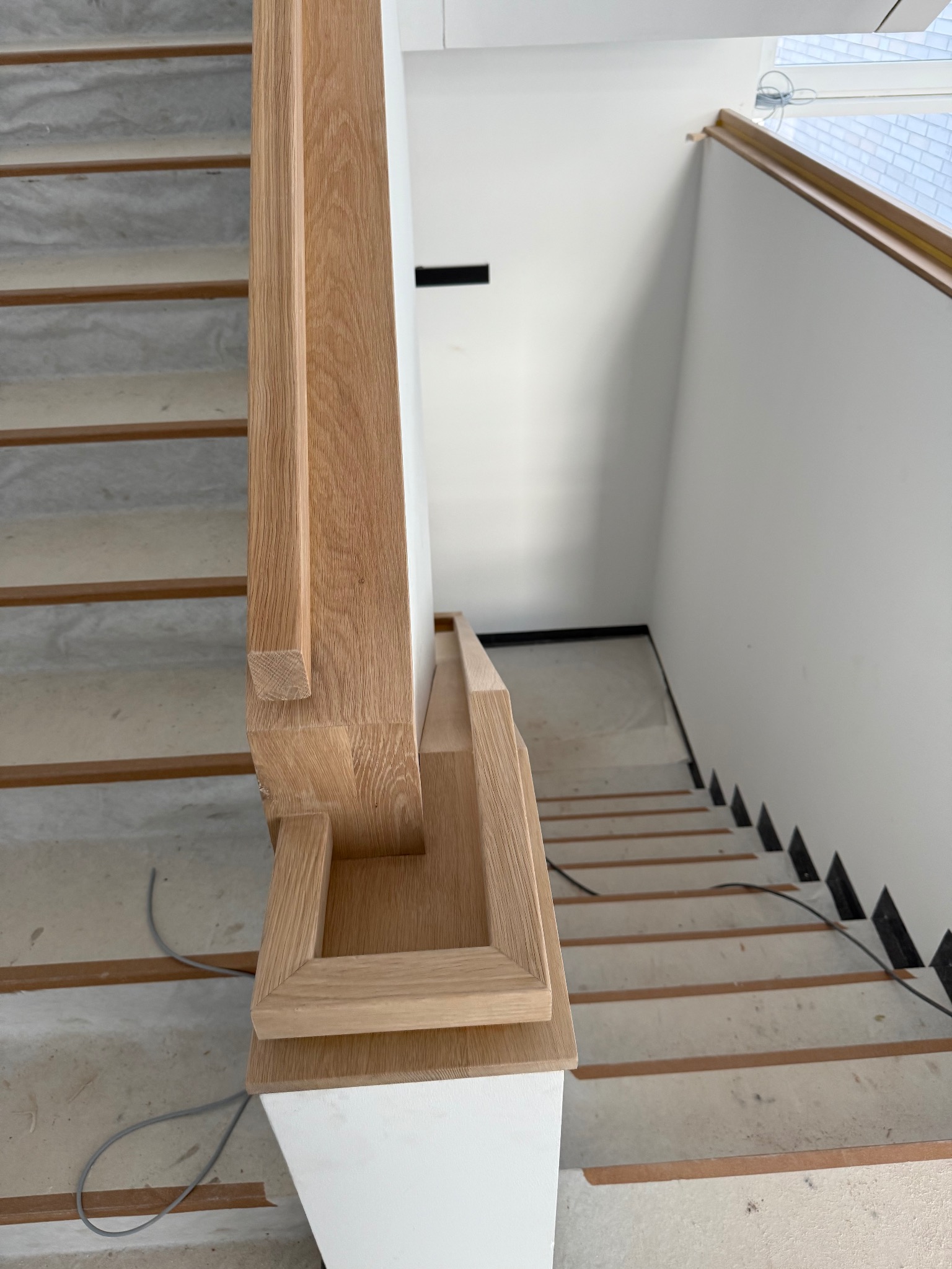 Jasne drewniane schody z białymi podstopnicami, widok z góry, ukazujący detale poręczy i wykończenia, w nowoczesnym, minimalistycznym wnętrzu.