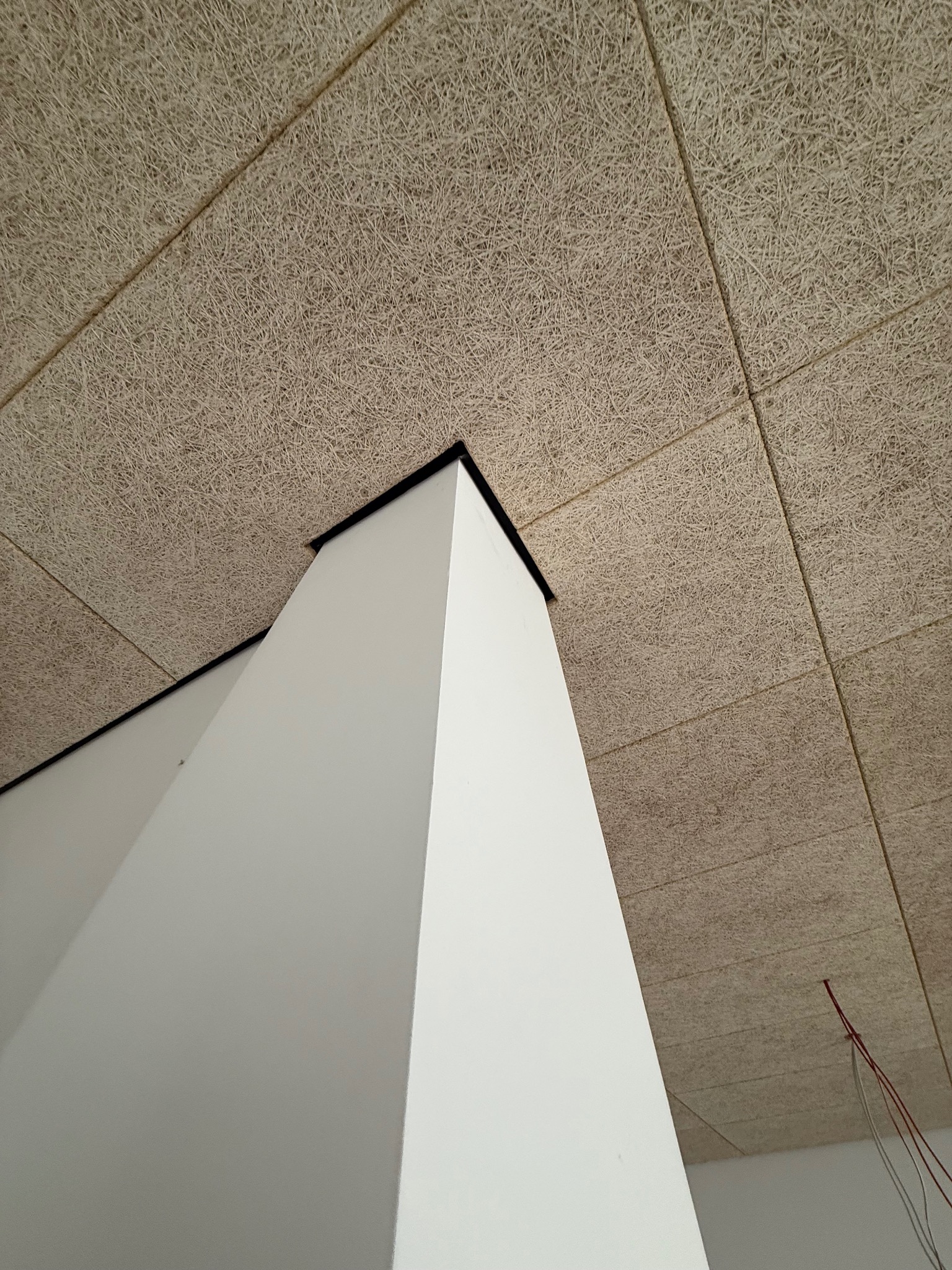 Panel sufitowy z włókien drzewnych, zamontowany na konstrukcji, widok z dołu, z fragmentem białej ściany i wystającymi przewodami elektrycznymi.