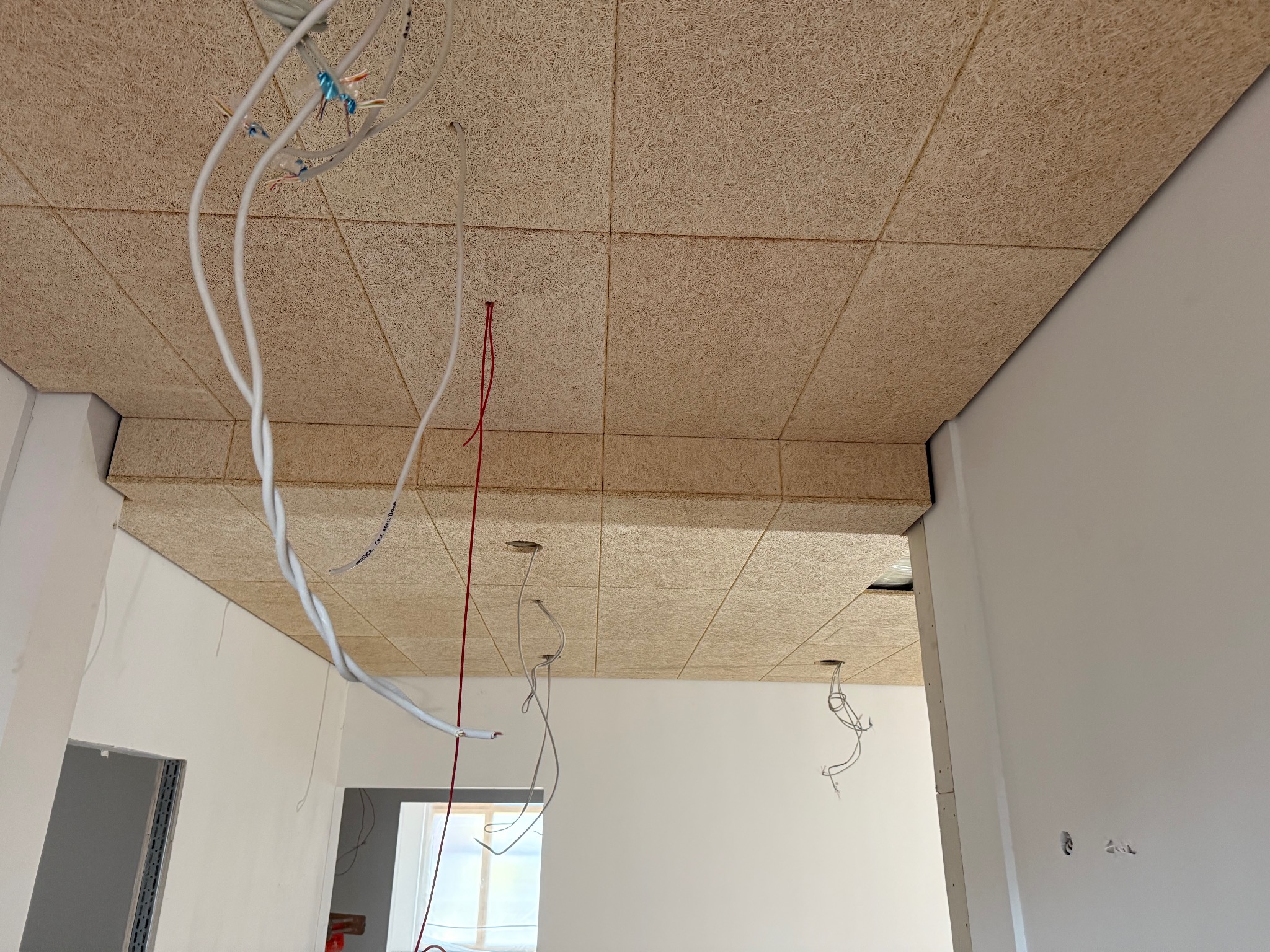 Montaż sufitu z paneli drewnopochodnych z widoczną instalacją elektryczną w nowym wnętrzu. Widok na sufit i białe ściany w trakcie prac wykończeniowych.