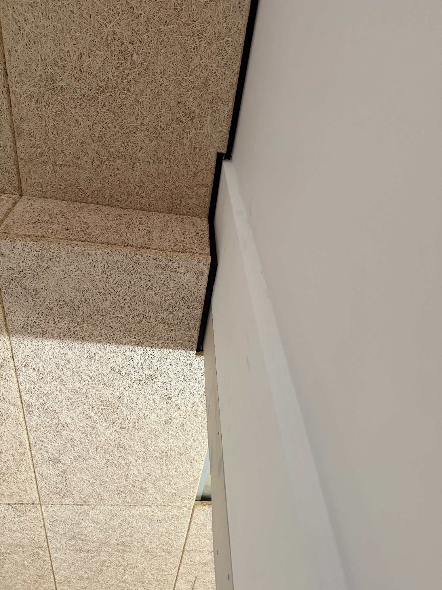 Fragment wykończenia wnętrza: płyty z włókna drzewnego na suficie i ścianie, połączone czarną listwą. Minimalistyczne połączenie faktur i kolorów.