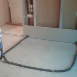 Instalacja przewodów elektrycznych w peszlu, mocowanych do podłoża metalowymi uchwytami, w surowym stanie budynku, z widocznymi elementami konstrukcji ścian.