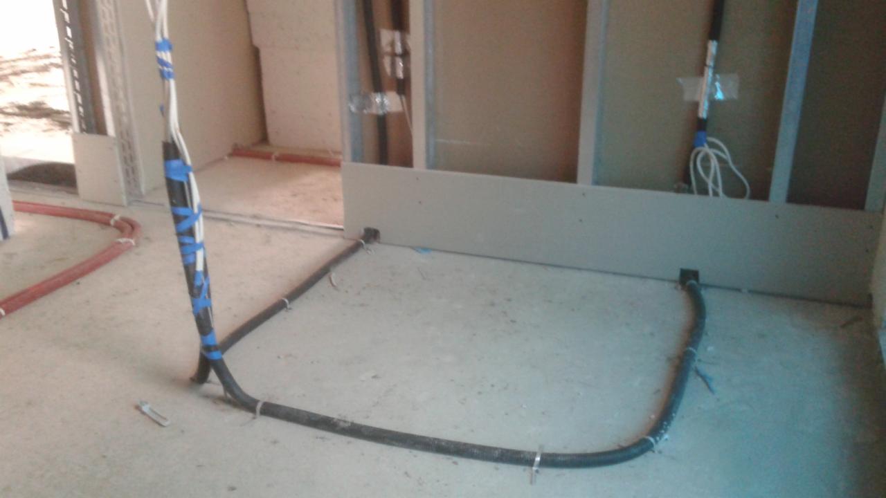 Instalacja przewodów elektrycznych w peszlu, mocowanych do podłoża metalowymi uchwytami, w surowym stanie budynku, z widocznymi elementami konstrukcji ścian.