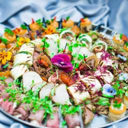 Niku Bowling Monika Gościniak - Dekoracyjna srebrna taca z różnorodnymi przekąskami: roladki z grillowanej cukinii, mini tortille z mięsem, roladki z wędlin, mini tartaletki z kremem, udekorowane świeżymi kwiatami i mikro-ziołami...