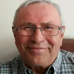 Portret uśmiechniętego, starszego mężczyzny w okularach i koszuli w kratę na jasnym tle, prawdopodobnie geologa.