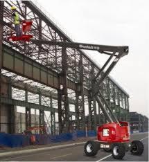 Czerwona platforma robocza Manlift 85 z wysięgnikiem teleskopowym unosi dwóch pracowników w kamizelkach odblaskowych na tle konstrukcji stalowej hali.