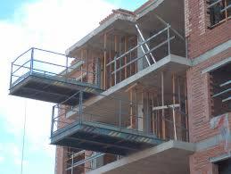 Budynek w trakcie rozbiórki, z widocznymi elementami konstrukcyjnymi i rusztowaniami, ceglana elewacja w trakcie demontażu, niebo w tle.