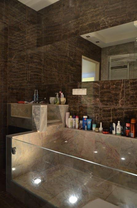 Wykończona łazienka z ciemnymi, marmurkowymi płytkami, szklaną obudową wanny i półką na kosmetyki.