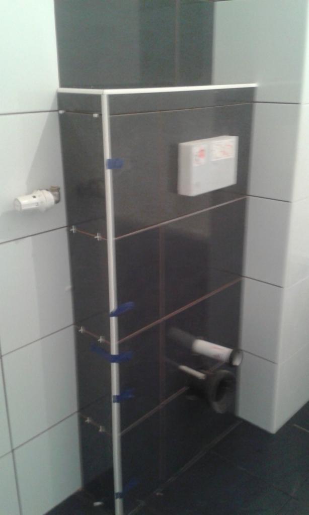 Montaż czarnych płytek ceramicznych na zabudowie stelaża WC, widoczne listwy wyrównujące i krzyżyki dystansowe.