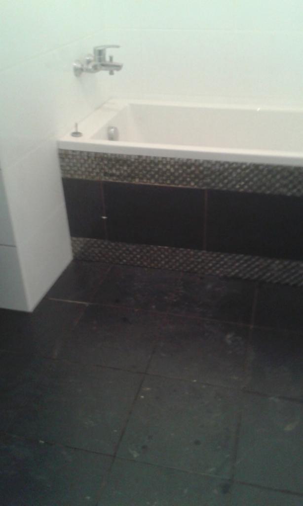 Wykończona łazienka z czarnymi płytkami podłogowymi i obudową wanny z dekoracyjnym pasem mozaiki.