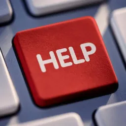 Czerwony klawisz z napisem 'HELP' na klawiaturze komputera, otoczony szarymi klawiszami. Klawisz pomocy jest lekko wciśnięty, co sugeruje jego użycie.
