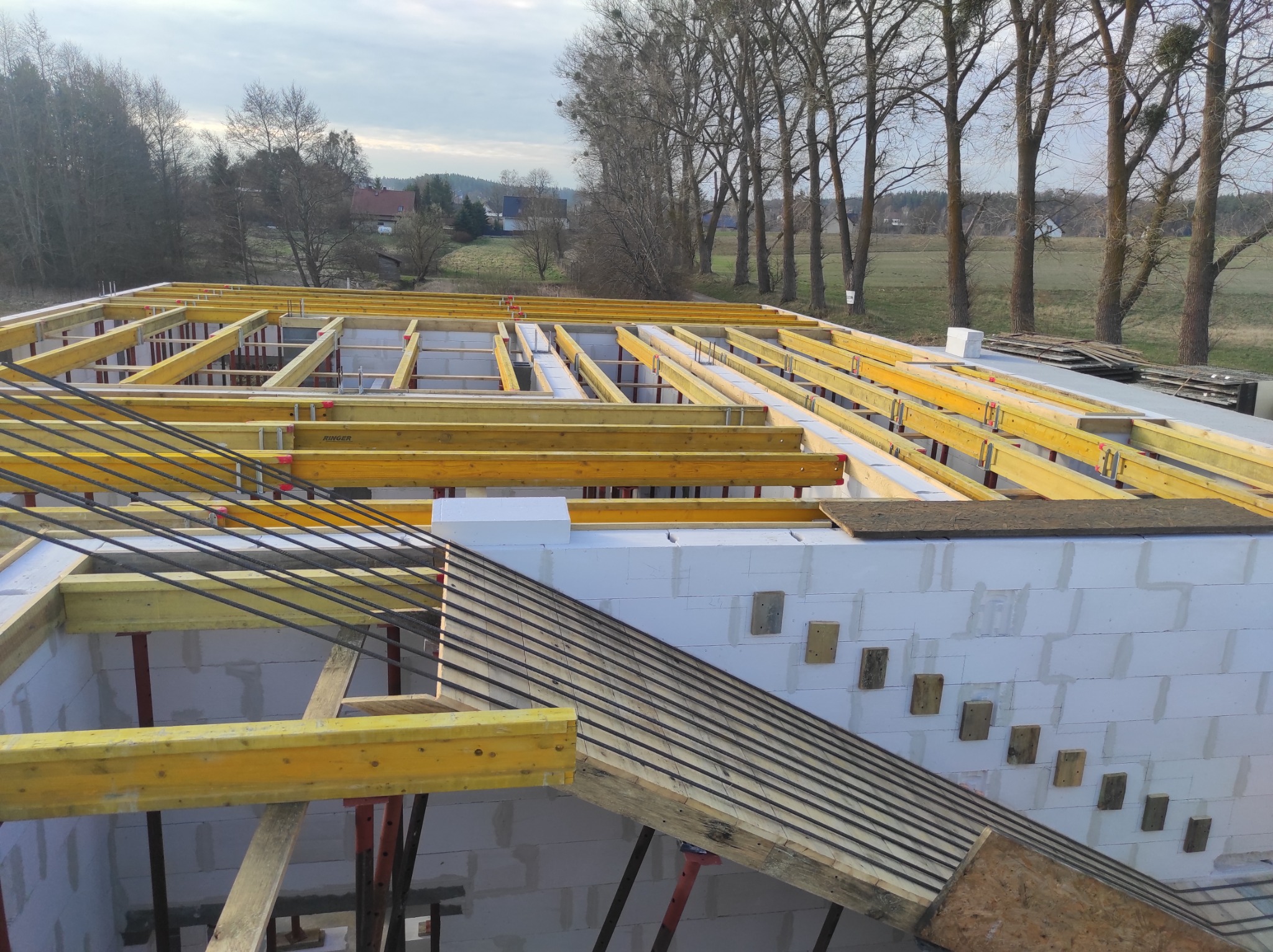 Wznoszenie ścian z białych bloczków i szalunku stropu z żółtych belek na budowie domu jednorodzinnego, widok z góry na konstrukcję w trakcie realizacji.