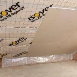 Ocieplenie poddasza wełną mineralną Isover, folia paroizolacyjna Vario KM Duplex UV i płyta karton-gips na skośnej powierzchni poddasza, widoczny fragment ściany z cegły.