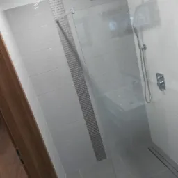 Nowoczesna kabina prysznicowa typu walk-in z szarą armaturą, wykończona płytkami w odcieniach szarości z dekoracyjnym pasem mozaiki.