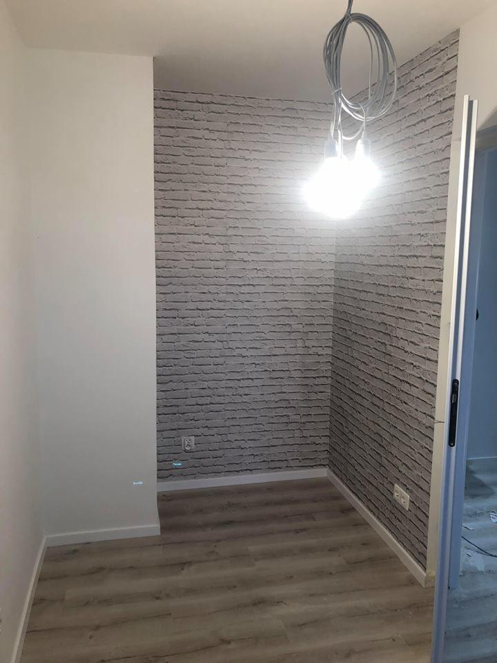 Wnęka w pokoju z wykończoną ścianą imitującą cegłę, podwieszonymi przewodami z żarówkami i panelami na podłodze.