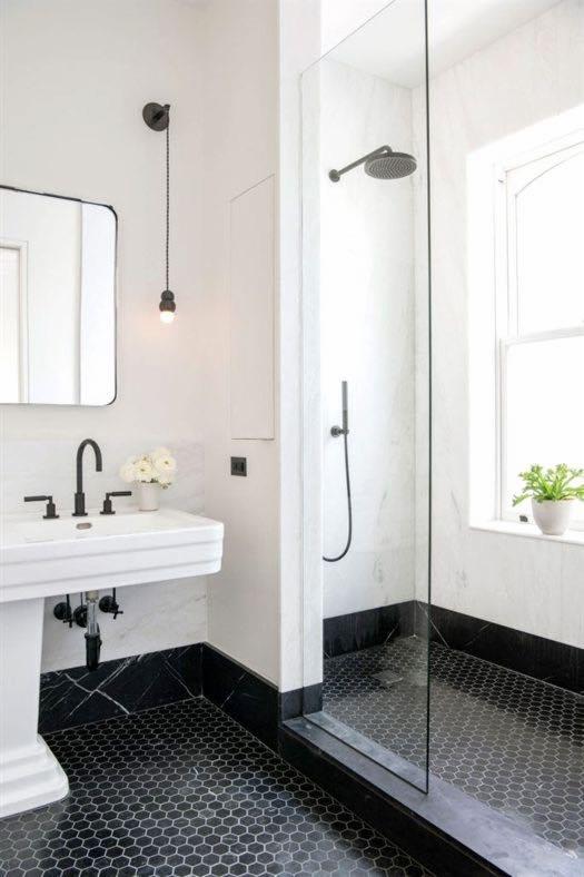 Elegancka łazienka z czarno-białą mozaiką heksagonalną na podłodze, dużą kabiną prysznicową ze szklaną ścianką, umywalką na postumencie, minimalistycznym lustrem i wiszącą lampą na sznurku.