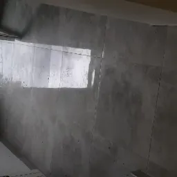 Ułożone szare płytki podłogowe w nowym pomieszczeniu, widoczne przez otwarte drzwi zieleń i ulica.