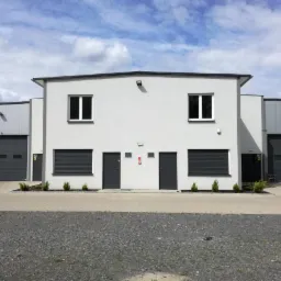 Nowoczesny budynek magazynowo-biurowy z szarymi bramami segmentowymi i roletami antywłamaniowymi, oświetlony jasnym, naturalnym światłem.