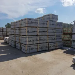 Płyty drogowe z betonu architektonicznego w szarym odcieniu, ułożone w stosy na paletach w Bystrej, gotowe do transportu, widoczne na placu składowym pod błękitnym niebem.