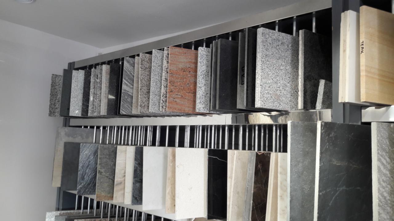 Ekspozycja próbek różnych rodzajów kamienia na metalowym stojaku w sklepie, widoczne różne kolory i wzory.