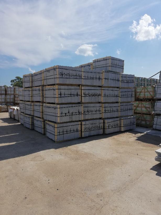 Płyty drogowe z betonu architektonicznego w szarym odcieniu, ułożone w stosy na paletach w Bystrej, gotowe do transportu, widoczne na placu składowym pod błękitnym niebem.